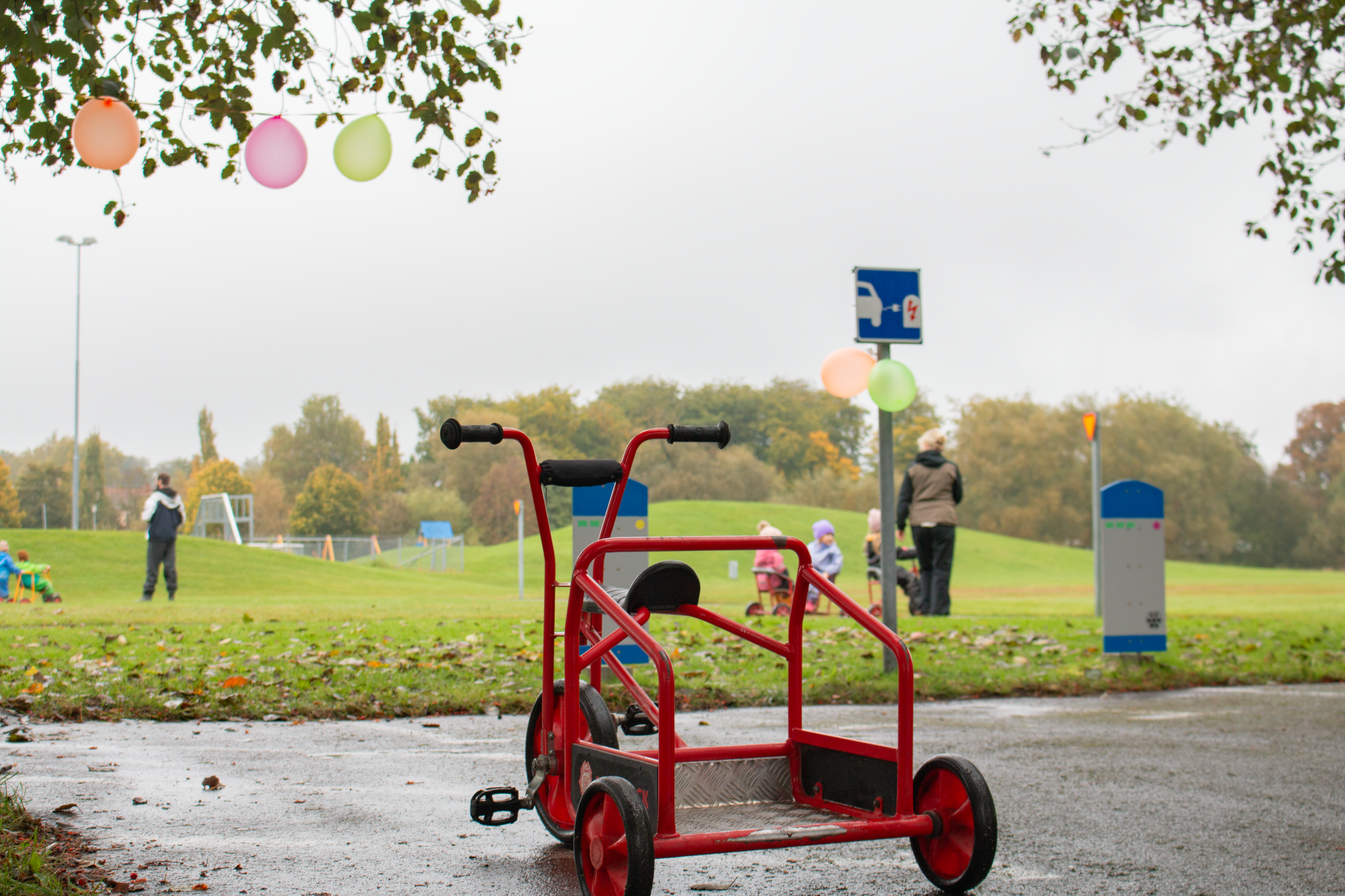 röd trehjuling i förgrunden. I Bakgrunden syns barn cykla på trehjulingar.