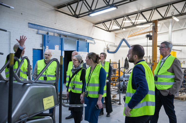 en grupp av människor står inne i en verkstad och lyssnar på en man som pratar.