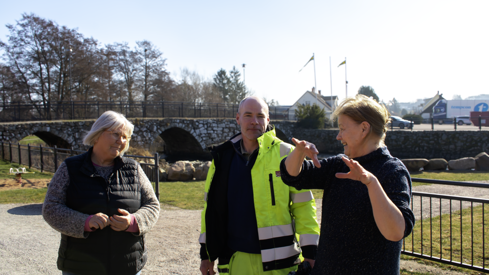 Två personer lyssnar på en tredje person prata, utomhus, vid parken.