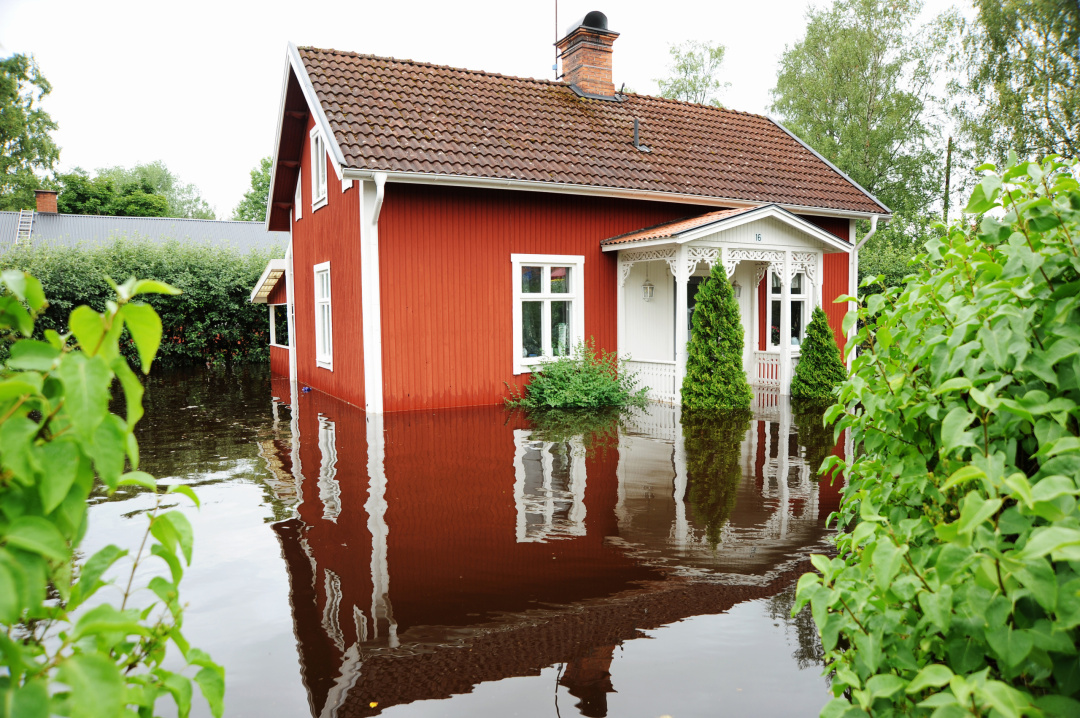 röd stuga med vita knutar som står med vatten ända upp till träfasaden