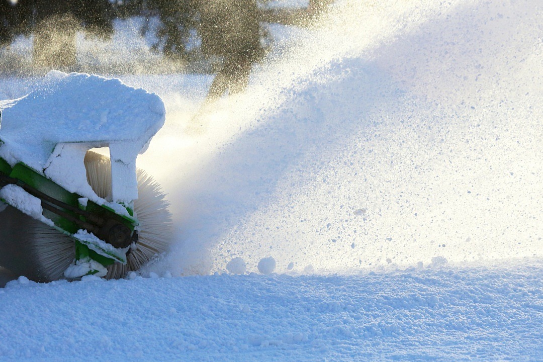 Närbild på snö och del av ett snöröjningsfordon.